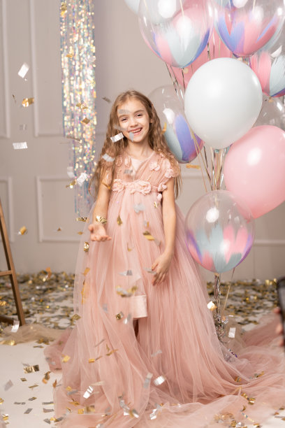 一个身穿优雅薄纱裙的快乐女婴站在气球的背景下微笑着庆祝她的生日。图片下载