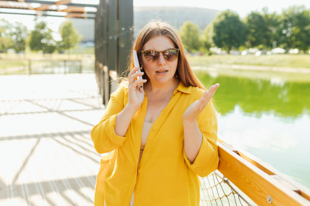心烦的年轻女人在电话里失望地听到坏消息，悲伤忧郁的女孩说有不愉快的智能手机谈话在河背景。负面情绪。女性在公园前摆姿势拍照图片下载