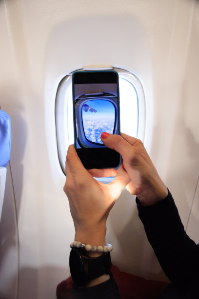 通过舷窗用智能手机拍下云层和飞机机翼图片下载