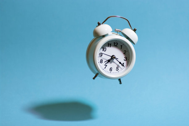 白色复古风格的闹钟在蓝色背景上飞翔，投下坚硬的阴影。飞行模拟时钟。图片下载