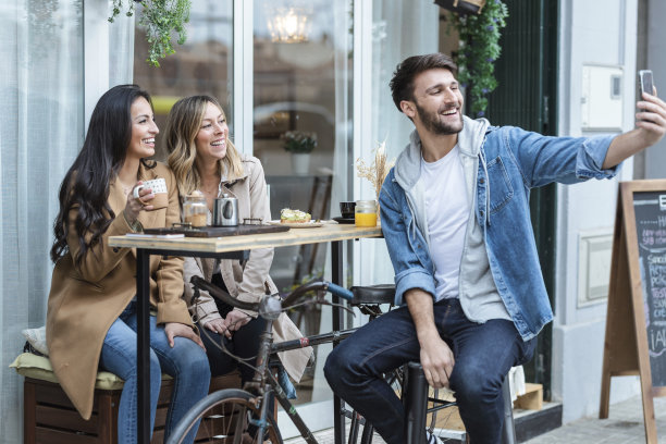 一群酷炫的朋友在健康的咖啡馆露台上一边分享早午餐，一边用智能手机自拍。图片下载