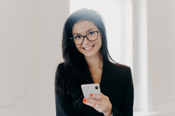 快乐的商务顾问穿着正装，拿着手机，发短信，上网看新闻，在办公室室内摆姿势，有辛苦工作的一天。人、科技、创业理念图片下载