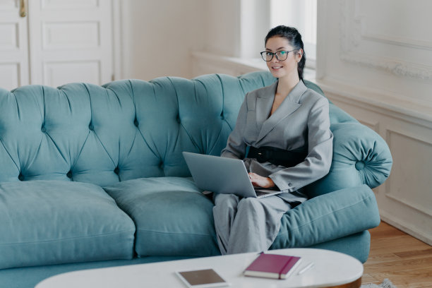 当代成功的女商人在宽敞的房间里舒适的沙发上摆姿势，阅读有用的商业发展文章，在笔记本电脑上工作，穿着优雅的衣服图片下载