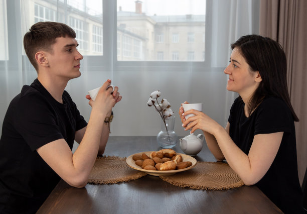 男人和女人拿着咖啡杯看着对方。年轻夫妇的早餐在餐桌上。有选择性的重点。图片为网站关于家庭，食物。图片下载