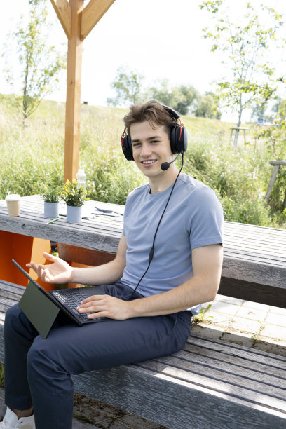 很酷，穿着灰色衬衫的年轻人戴着耳机坐在公园的户外图片下载