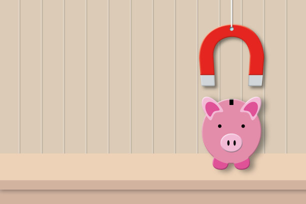 桌子上红色的磁铁吸引存钱罐，木制背景隐喻吸引投资的概念。图片下载