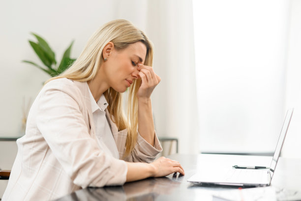 疲惫的女性感觉无聊和疲惫。迷人的金发女人闭着眼睛坐在笔记本电脑前图片下载