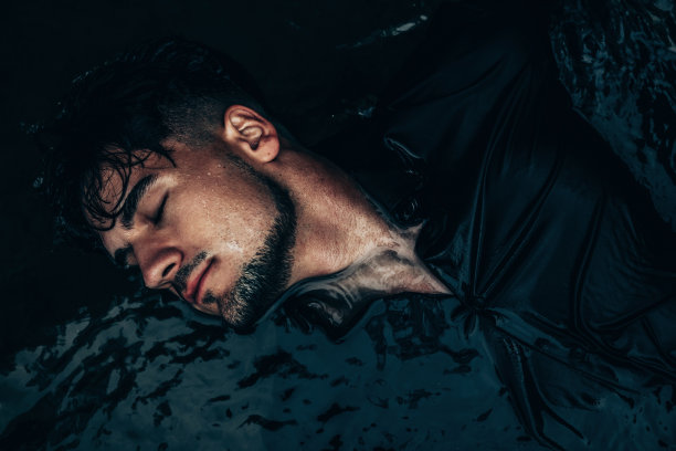 一个穿着黑衬衫的男人闭着眼睛躺在水里的画像图片下载