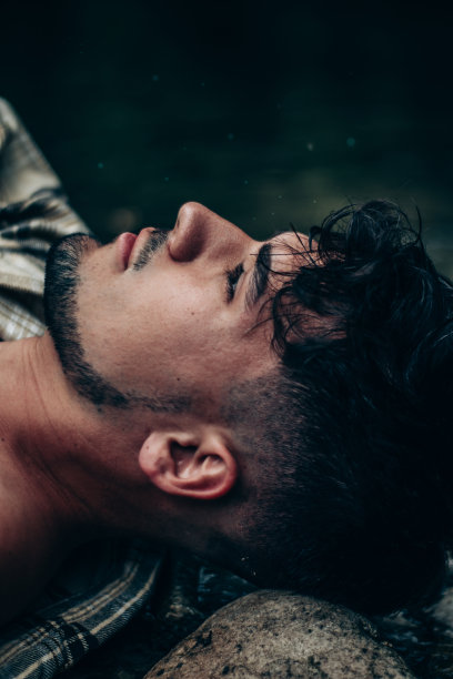 一个穿着格子衬衫的男人躺在河中的岩石上，看着远处图片下载