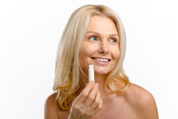 快乐和乐观美丽的中年妇女应用天然的润唇膏隔离在白色。迷人的金发女士使用保湿唇膏，治疗膏图片下载