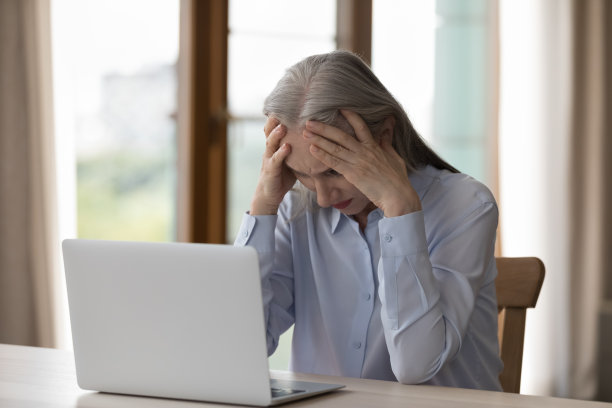 年长的女商人看着笔记本电脑抱着头看起来很绝望图片下载