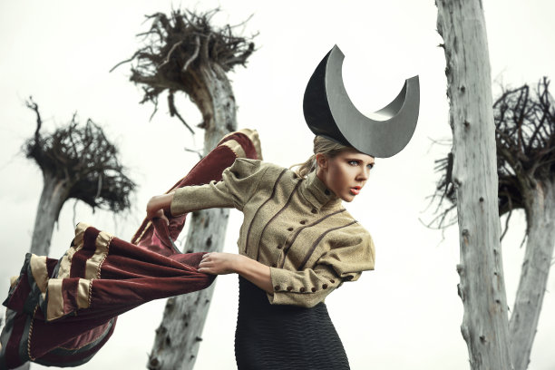 美丽的金发女斗牛士直勾勾地看着她的前面，在一个宽阔的运动摇摆着红色的斗篷，在倒立的树前面图片下载