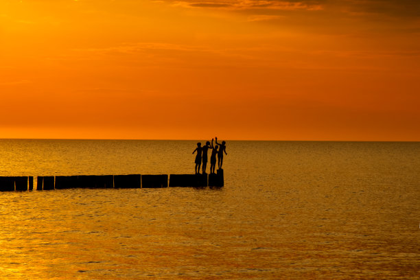 四个十几岁的孩子的剪影站在防波堤和橙色的日落图片下载