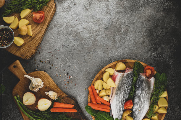 俯视未煮熟的生鱼鲈鱼和切好的蔬菜放在一块木板上准备烹饪。素食的概念。图片下载