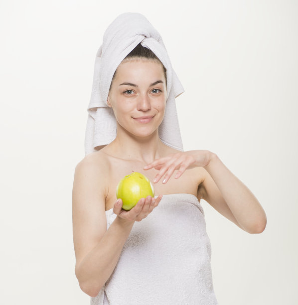 一幅美丽的肖像，一个开朗的女孩用毛巾在她的头上孤立。面部皮肤护理与健康理念。白底特写。女孩拿着杯子拿着苹果刷牙做面膜图片下载