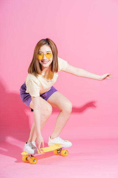亚洲少女的照片与滑板在粉红色的背景图片下载