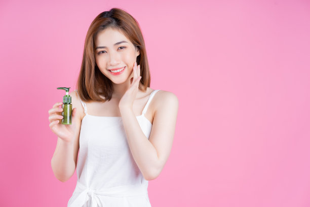 年轻的亚洲女子拿着喷瓶在粉红色的背景上的图像图片下载