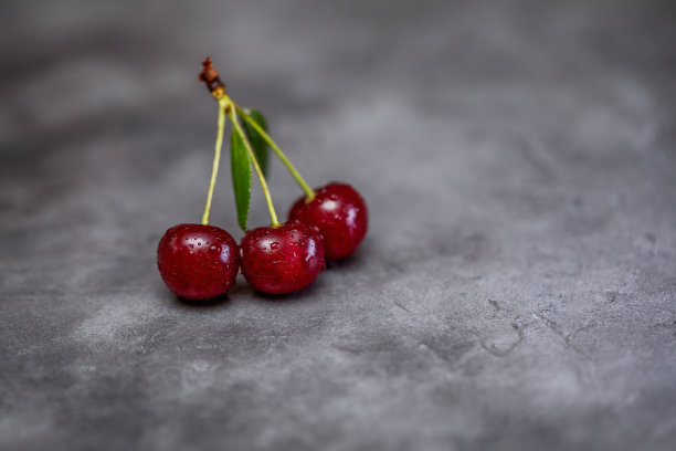 成熟樱桃的红色浆果，绿叶在黑色的工艺背景。浆果的特写照片。图片下载