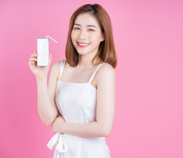 年轻的亚洲女人拿着牛奶盒的形象在粉红色的背景图片下载