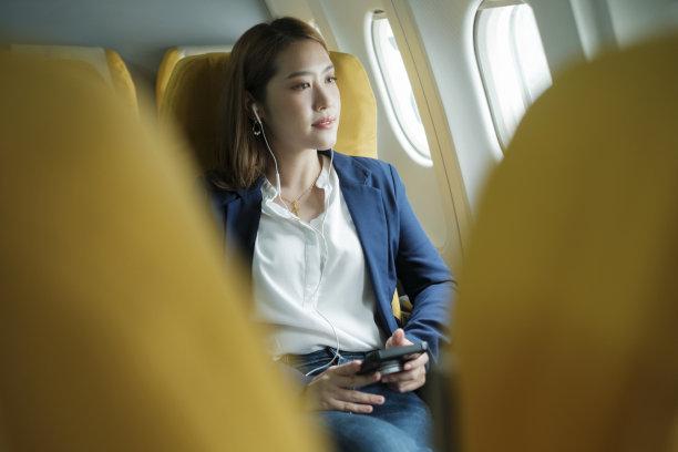 商务女性在飞机上，工作时使用手机。耳机图片下载