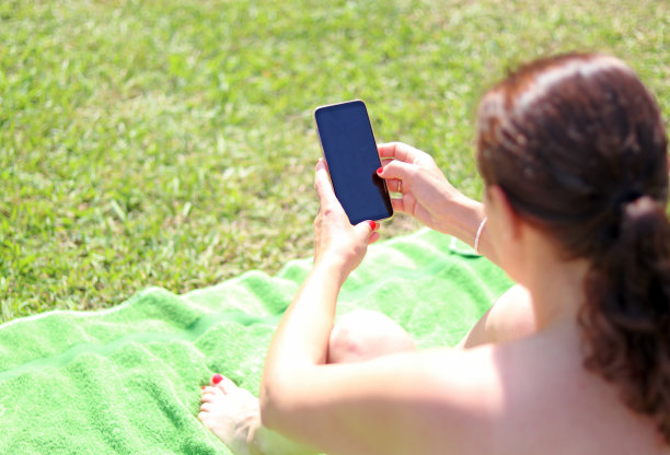 年轻女子晒日光浴看手机图片下载