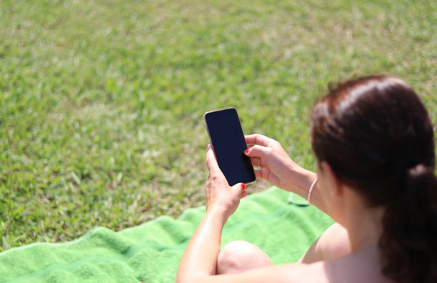 年轻女子晒日光浴看手机图片下载