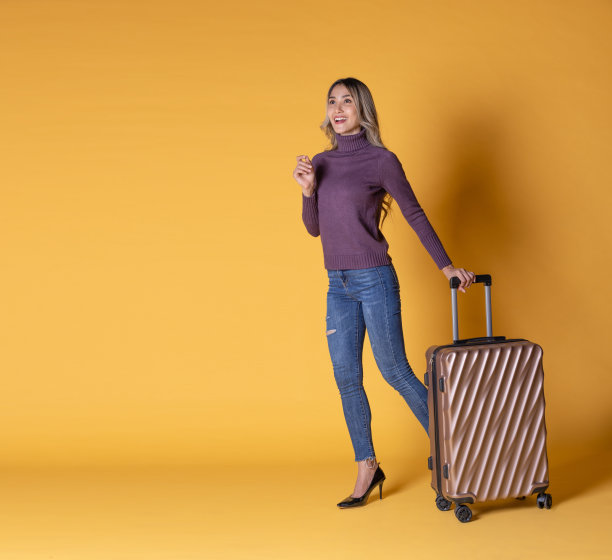 漂亮的年轻女子与手提箱和手提包孤立的黄色背景图片下载