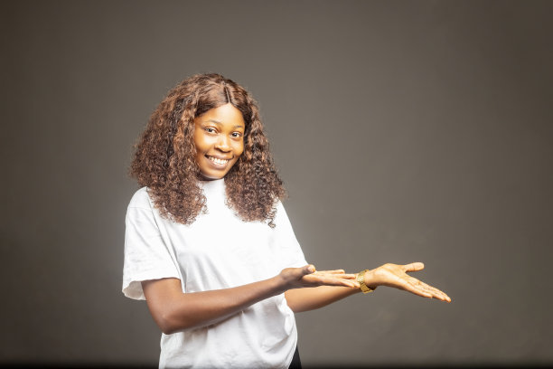 年轻的非裔美国妇女孤立在灰色背景向一边伸出手来邀请。广告的概念图片下载