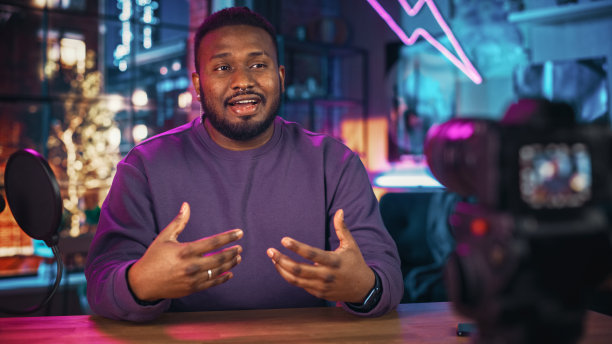 时髦的年轻非洲裔美国人对着麦克风说话，而录音节目从他的阁楼公寓。快乐的黑人男性在摄像机和录制播客上社交媒体直播。图片下载