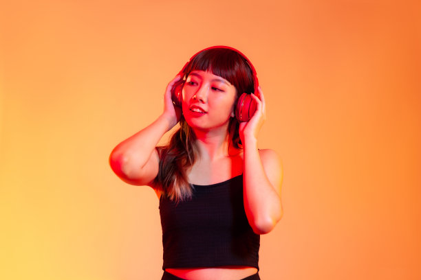 年轻的亚洲女子长头发，黑色背心，戴着红色耳机听音乐在橙色的背景图片下载