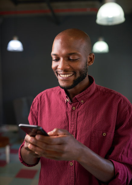 一个有魅力的黑人男子在他的手机上发短信，微笑着图片下载