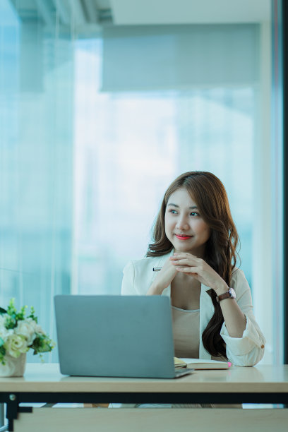 一个迷人的年轻亚洲女商人在她的办公桌上用笔记本电脑工作。垂直图图片下载