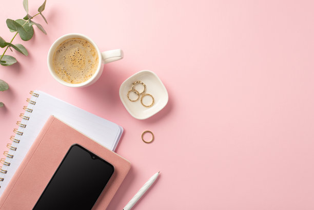 经营理念。工作空间智能手机的顶部视图照片在粉红色的组织者钢笔金戒指杯咖啡和桉树在孤立的粉红色背景与copyspace图片下载