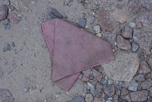 一条又旧又脏的红布披肩躺在灰色的沙子和小石头上图片下载