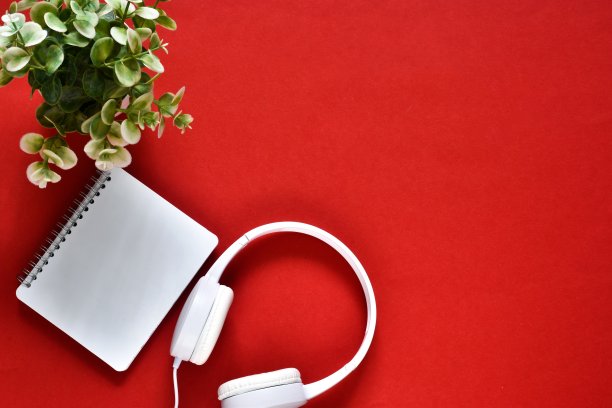 办公桌与耳机，绿色植物和笔在一个红色的背景图片下载