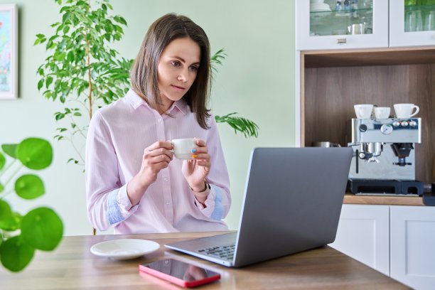 年轻女子坐在家里的厨房里使用笔记本电脑图片下载
