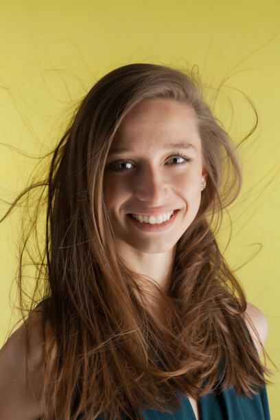 美丽的女孩与飘逸的头发在黄色的背景。深色头发的女士穿着漂亮的衬衫和牛仔裤在摄影棚里摆拍……图片下载