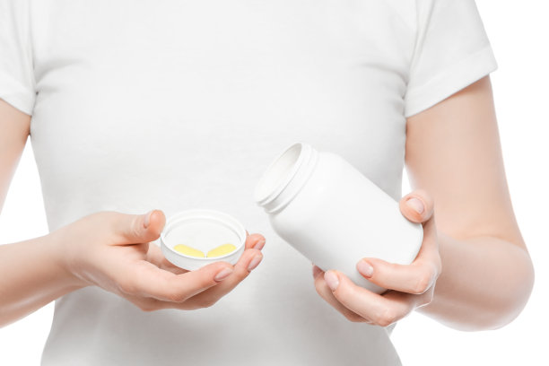 一个穿着白色t恤的女人从一个白色塑料瓶中倒进黄色药丸的镜头。孤立。图片下载