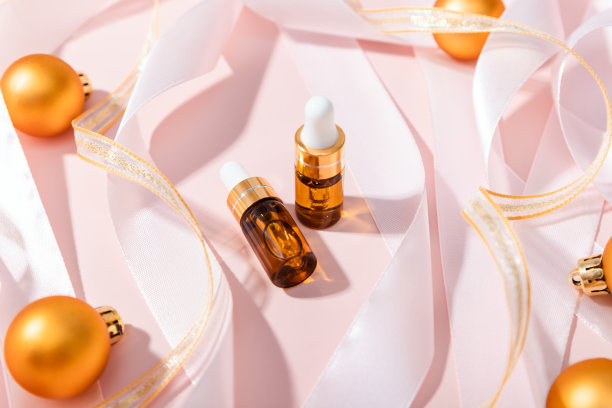 血清装在两个玻璃瓶里，配有吸管，丝带和粉色背景的圣诞球。精油、护肤、保湿美容产品。用于面部护理的美容产品。前面的顶视图。图片下载