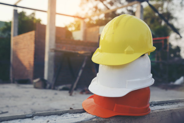 安全帽(安全帽)，用于工程师、安全员或建筑师，放置在水泥地面上，以砖为背景。施工现场的白、黄、橙安全帽(安全帽)。图片下载