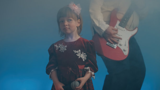 穿着复古礼服的小女孩在舞台上唱歌，她的父亲在弹奏电吉他图片下载