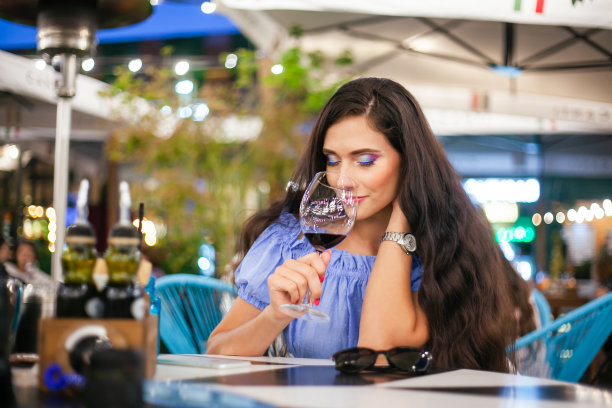 在街头咖啡馆里，一名化妆明亮的年轻女子从杯子里吸入葡萄酒的香气图片下载