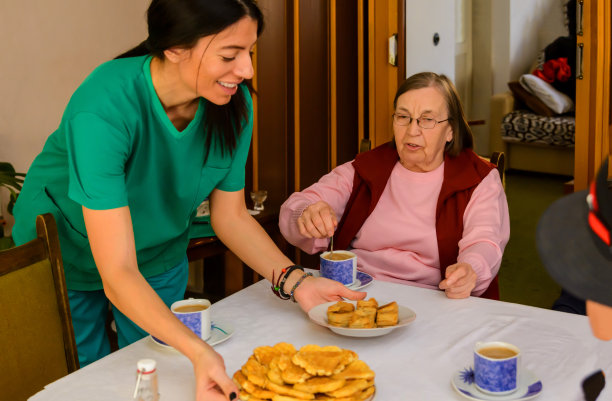 在一次社交聚会上，一位年轻的女看护为活跃的老年人提供食物。图片下载