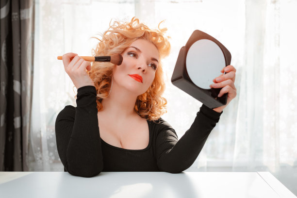 金发与复古的头发明亮的红色唇膏唇和化妆前镜。旧好莱坞看。肖像美丽的35-40岁女性迷人的庸俗形象图片下载