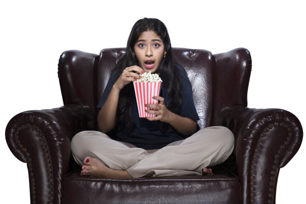 拿着爆米花的亚洲女人坐在沙发上，脸上带着恐惧的表情图片下载