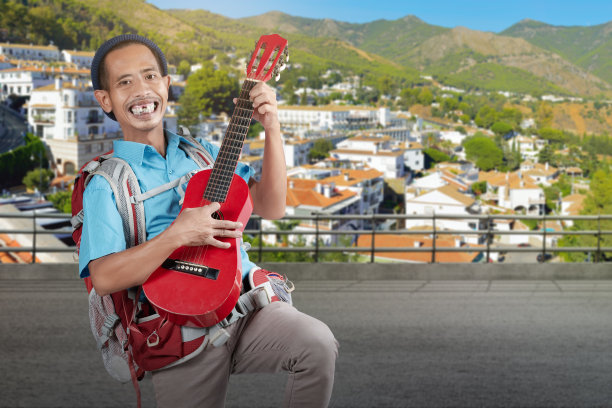 一名亚洲男子戴着一顶无檐帽，背着一个吉他背包站在街上图片下载