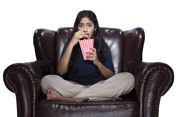 一名亚洲妇女坐在沙发上吃爆米花，脸上带着恐惧的表情图片下载