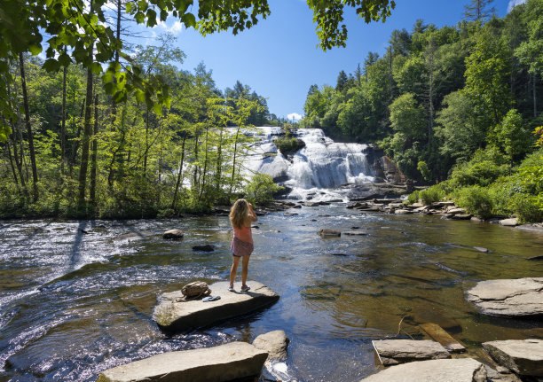 女孩站在岩石上欣赏美丽的瀑布景色。图片下载