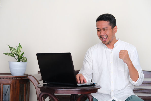 一名亚洲成年男子握紧拳头，兴奋地看着笔记本电脑图片下载
