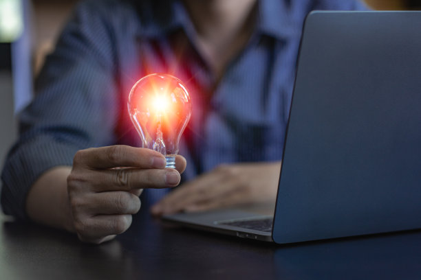 节能概念的商人拿着一个亮着灯的灯泡在笔记本电脑上图片下载